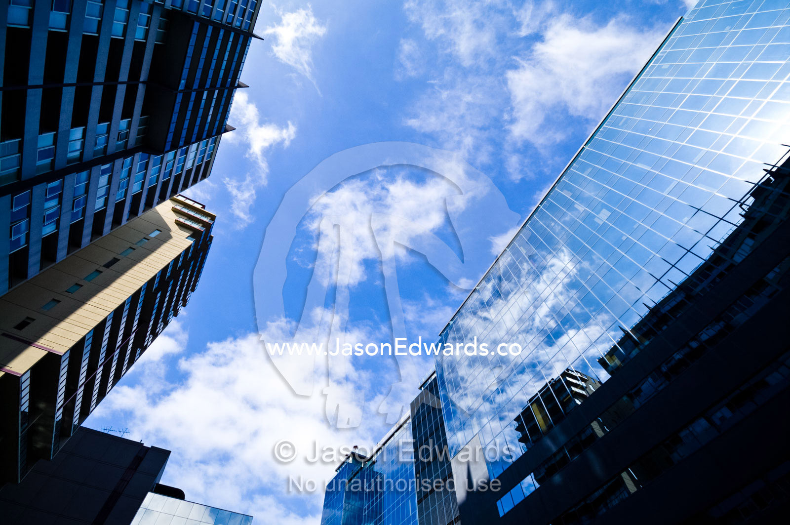 Blue sky and fluffy clouds reflect in the windows of an office block. St Kilda Road, Melbourne, Victoria, Australia.
