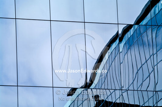 Office window panes reflect a building in distorted abstract curves. St Kilda Road, Melbourne, Victoria, Australia.