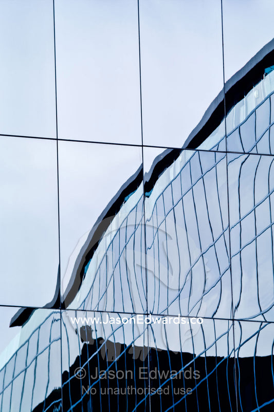 Office window panes reflect a building in distorted abstract curves. St Kilda Road, Melbourne, Victoria, Australia.
