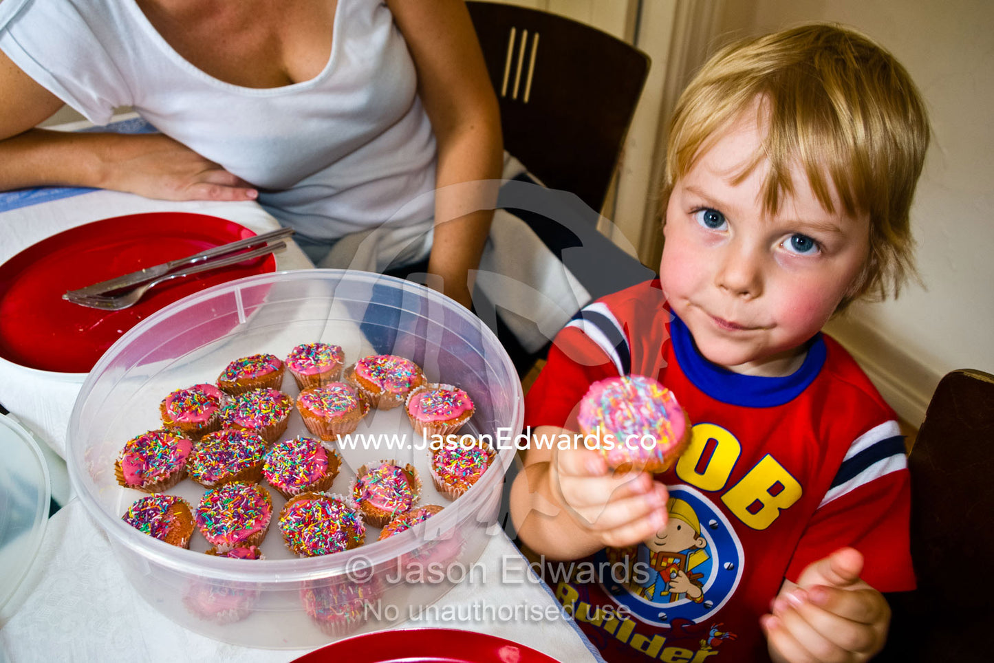A small boy offers a cupcake covered in colourful candy sprinkles. Carlton North, Melbourne, Victoria, Australia.