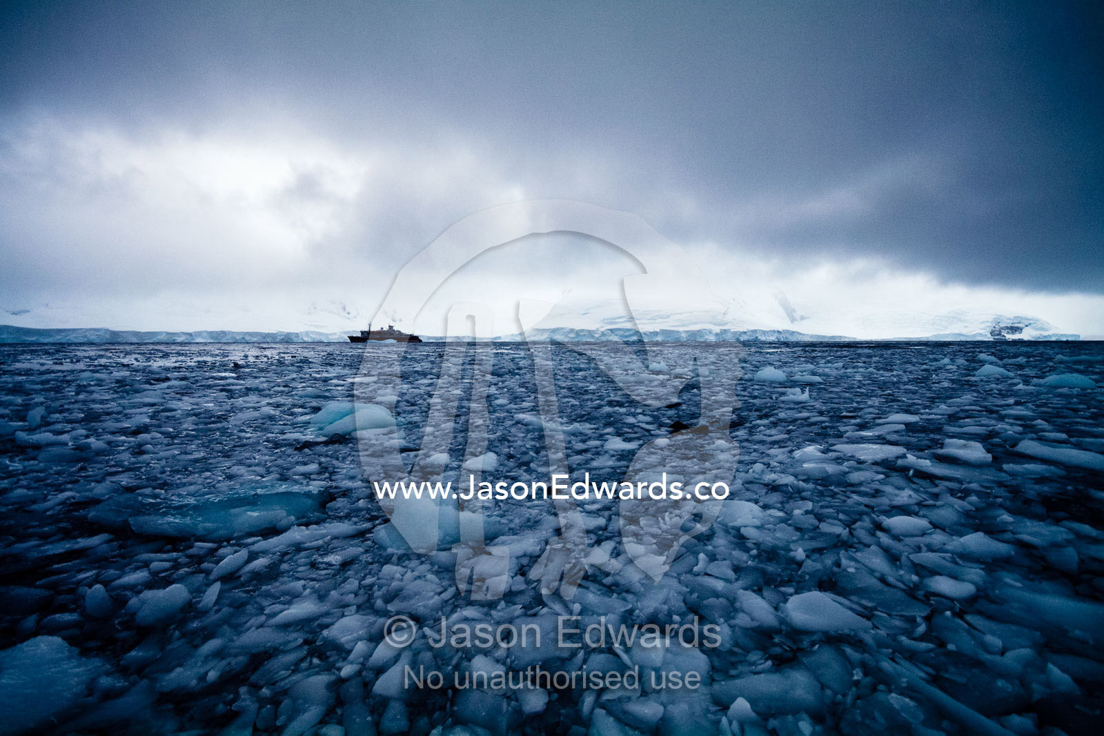Grey fractured ice engulfs an eco tourism ship on a bitter stormy day. Crystal Sound, Hanusse Bay, Antarctic Peninsula, Antarctic Circle, Antarctica.