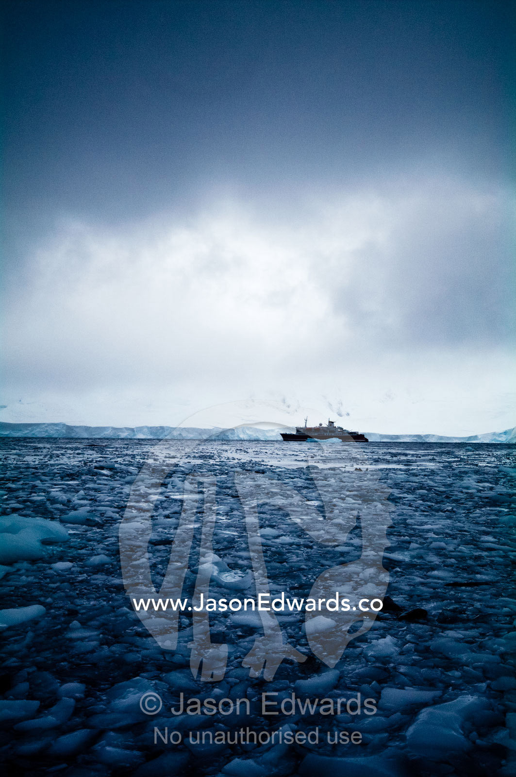 Grey fractured ice engulfs an ecotourism ship on a bitter stormy day. Crystal Sound, Hanusse Bay, Antarctic Peninsula, Antarctic Circle, Antarctica.