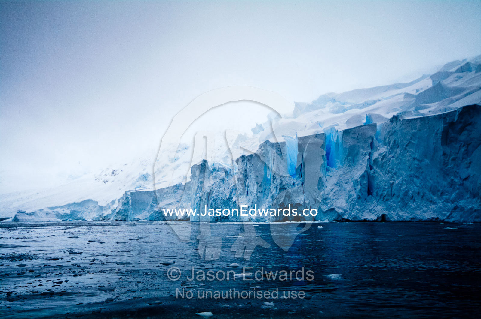 The fracture zone of massive glacial ice cliffs teeter over icy seas. Crystal Sound, Hansen Island, Hanusse Bay, Antarctic Peninsula, Antarctic Circle, Antarctica.