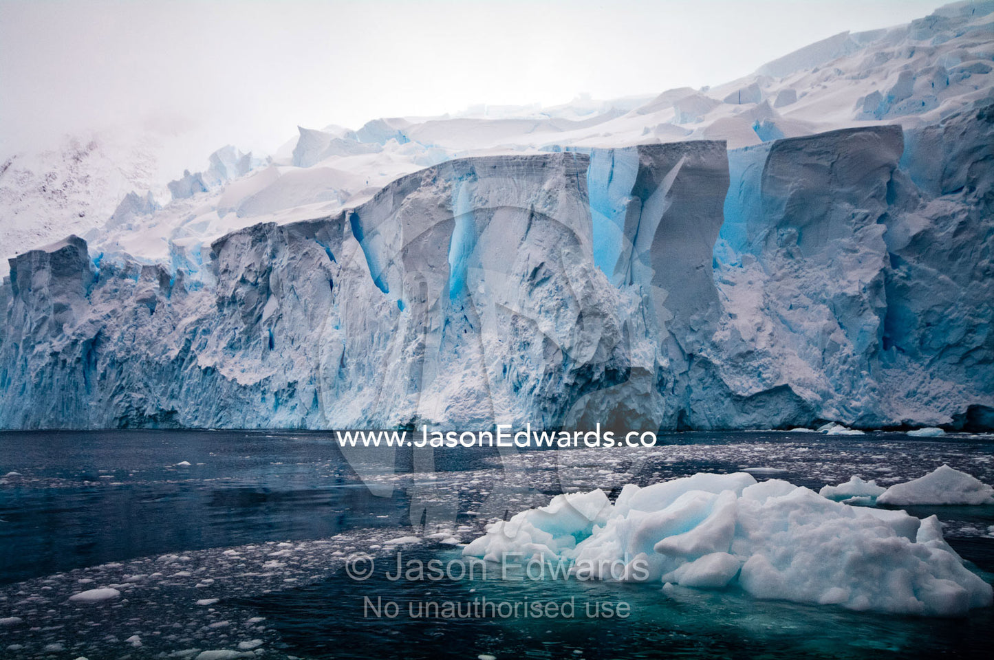 The fracture zone of massive glacial ice cliffs teeter over icy seas. Crystal Sound, Hansen Island, Hanusse Bay, Antarctic Peninsula, Antarctic Circle, Antarctica.