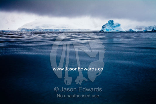 Under stormy skies an iceberg floats through mercury-like Frizzle Ice. Crystal Sound, Hanusse Bay, Antarctic Peninsula, Antarctic Circle, Antarctica.