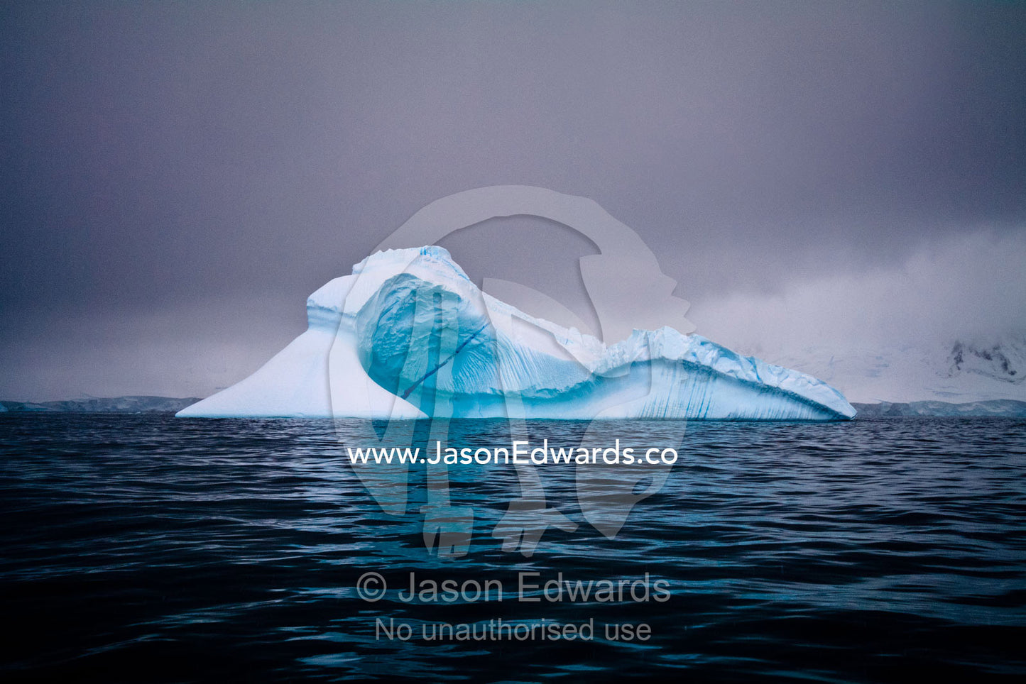 An iridescent iceberg floating in a dark sea beneath stormy skies. Crystal Sound, Hanusse Bay, Antarctic Peninsula, Antarctic Circle, Antarctica.