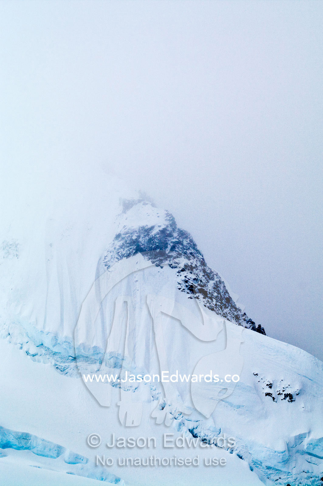 A jagged snow and ice encrusted mountain peak emerges from a storm. Crystal Sound, Hanusse Bay, Antarctic Peninsula, Antarctic Circle, Antarctica.