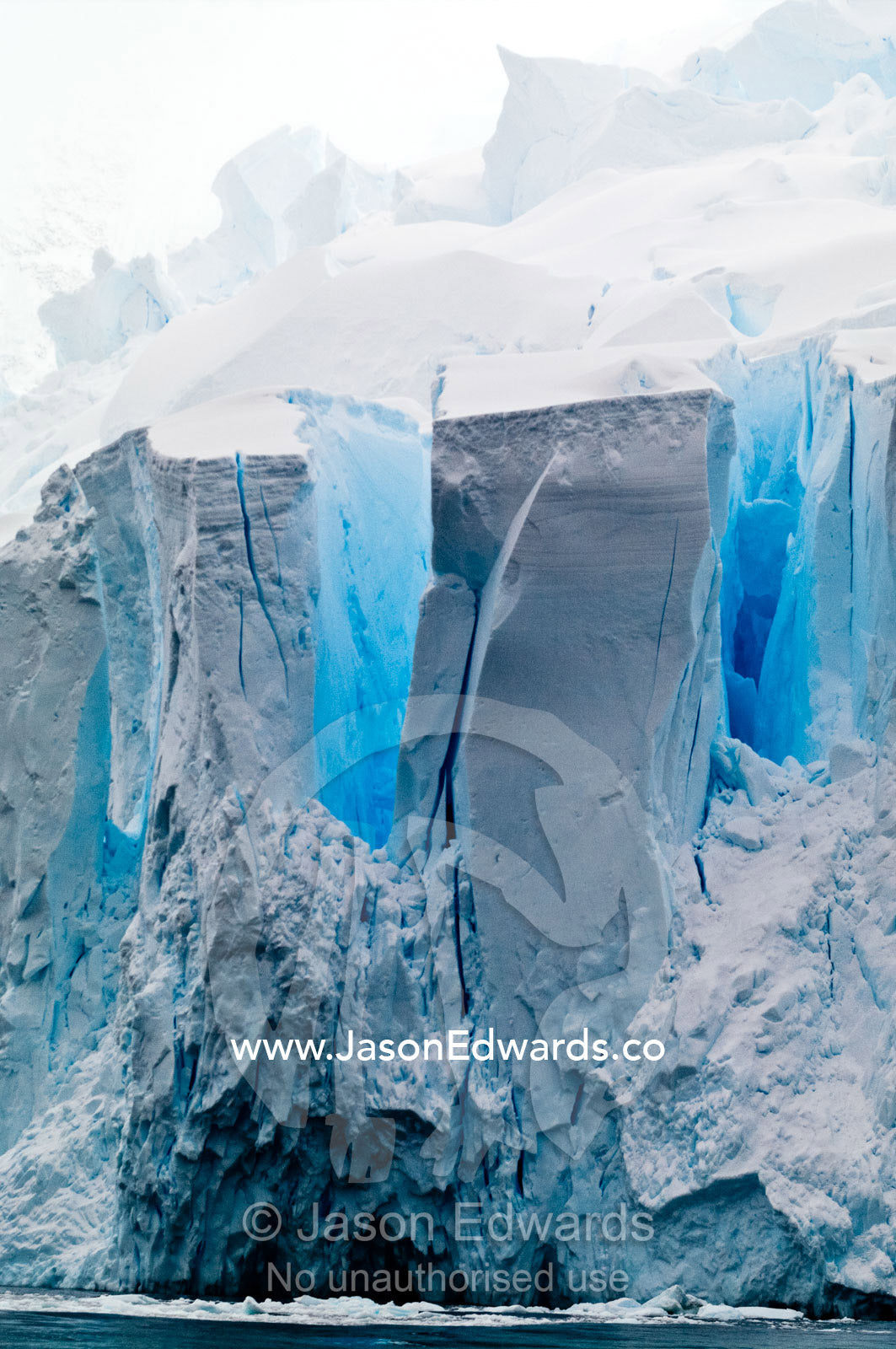 The fracture zone of massive glacial ice cliffs teeter over icy seas. Crystal Sound, Hansen Island, Hanusse Bay, Antarctic Peninsula, Antarctic Circle, Antarctica.