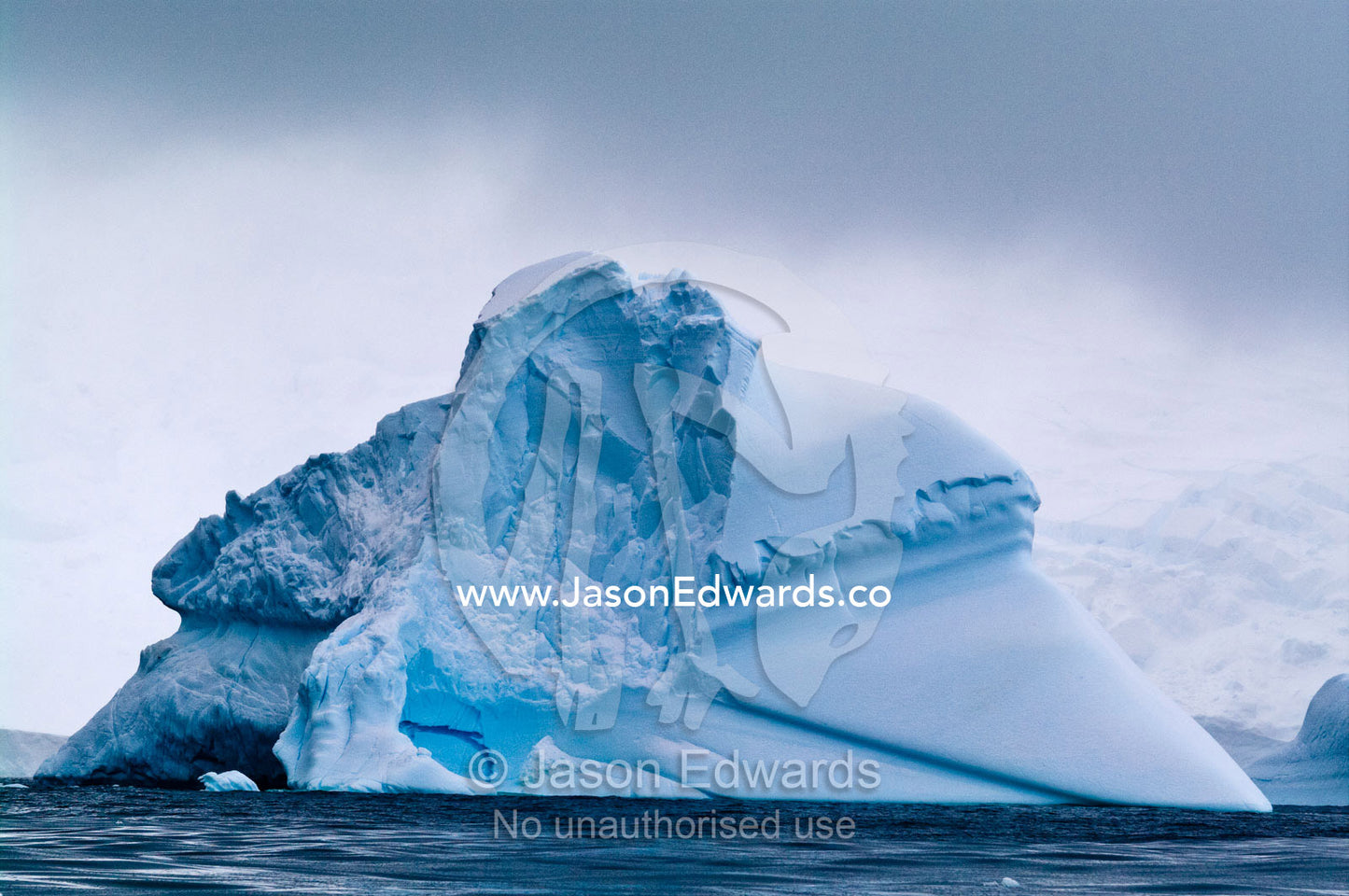 An enormous iceberg rises out of the sea beneath storm clouds. Crystal Sound, Hanusse Bay, Antarctic Peninsula, Antarctic Circle, Antarctica.