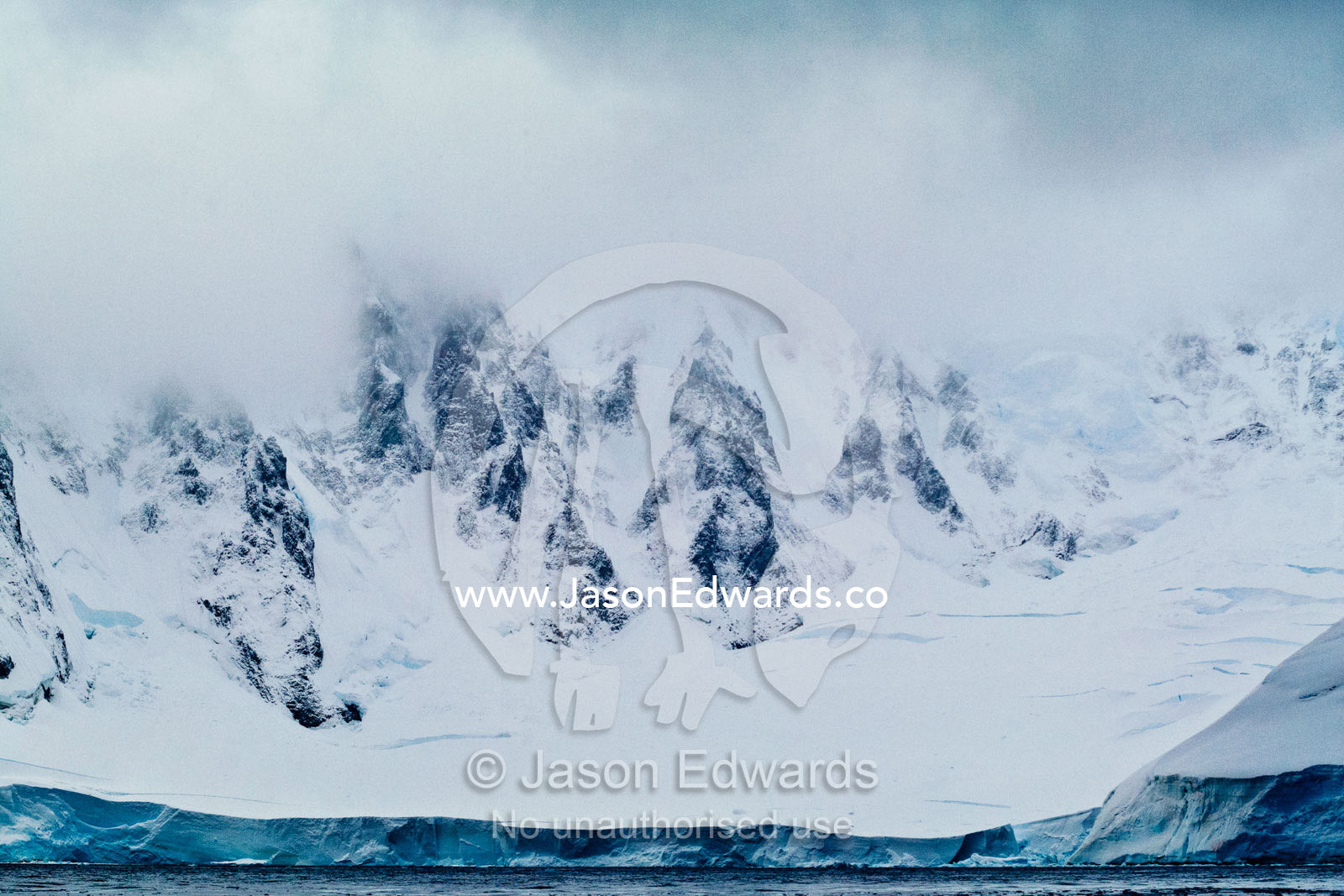Jagged peaks of a vast and menacing mountain range above a glacier. Crystal Sound, Hanusse Bay, Antarctic Peninsula, Antarctic Circle, Antarctica.