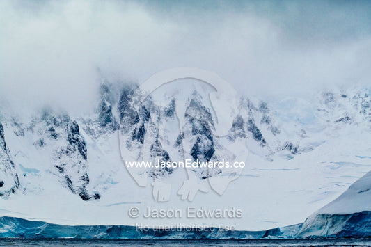 Jagged peaks of a vast and menacing mountain range above a glacier. Crystal Sound, Hanusse Bay, Antarctic Peninsula, Antarctic Circle, Antarctica.