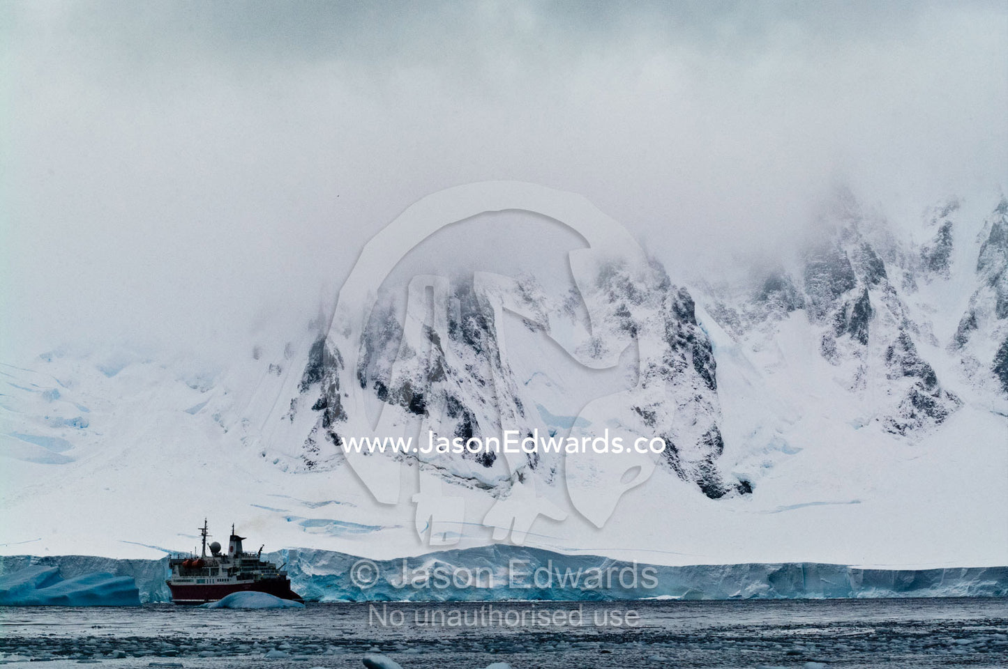 Vast and menacing mountains dwarf a glacier and ecotourism ship. Crystal Sound, Hanusse Bay, Antarctic Peninsula, Antarctic Circle, Antarctica.