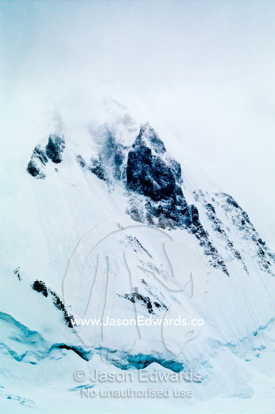 A jagged snow and ice encrusted mountain peak emerges from a storm. Crystal Sound, Hanusse Bay, Antarctic Peninsula, Antarctic Circle, Antarctica.