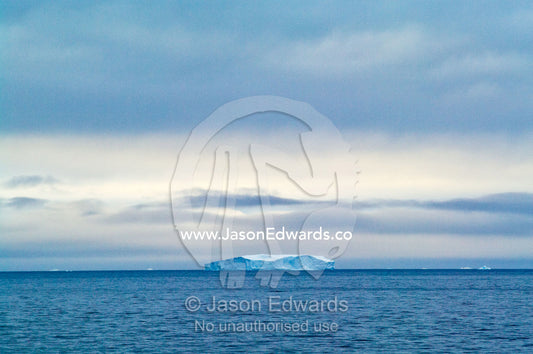 A lone iceberg floating in the open ocean after sunset. Crystal Sound, Antarctic Peninsula, Antarctic Circle, Antarctica.