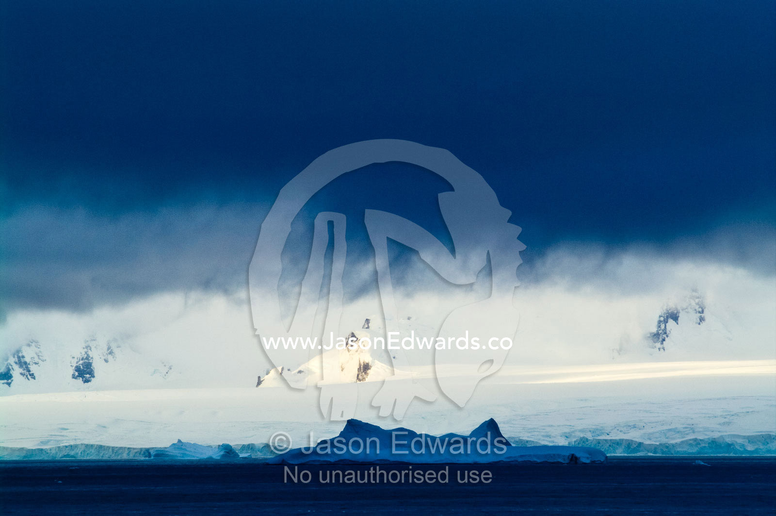 A dense storm descends over a mountain range dwarfing a large iceberg. Crystal Sound, Hanusse Bay, Antarctic Peninsula, Antarctic Circle, Antarctica.