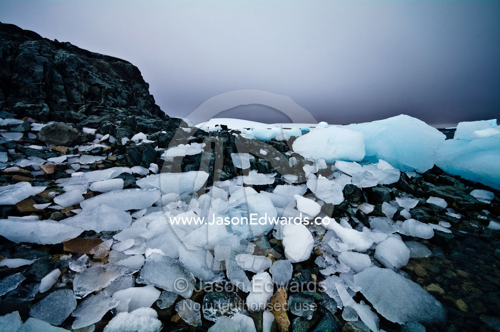 Ice boulders strewn over a rugged, stormy diorite beach and shoreline. Prospect Point, Crystal Sound, Antarctic Peninsula, Antarctic Circle, Antarctica.