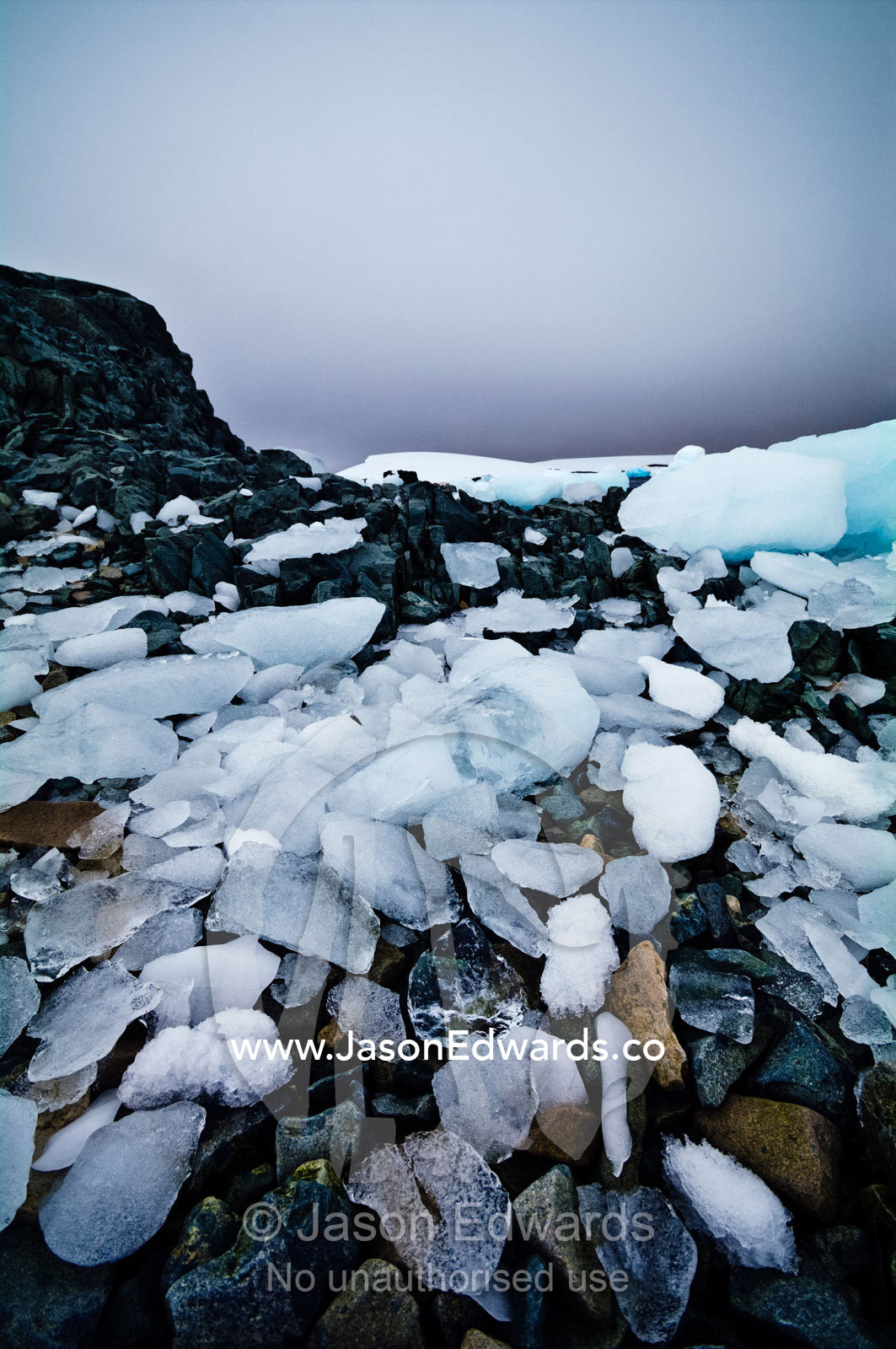 Ice boulders strewn over a rugged, stormy diorite beach and shoreline. Prospect Point, Crystal Sound, Antarctic Peninsula, Antarctic Circle, Antarctica.