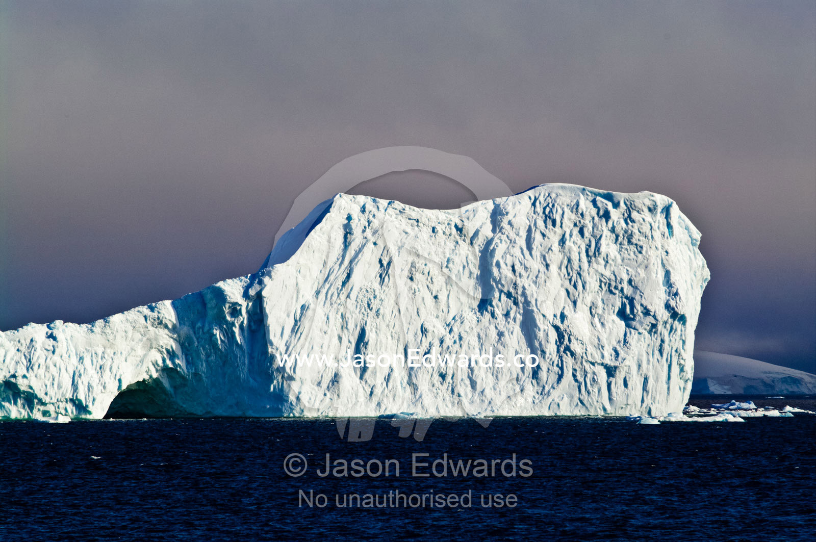 Sunlight bounces off the sheer rugged walls of an enormous iceberg. Fish Islands, Crystal Sound, Antarctic Peninsula, Antarctic Circle, Antarctica.