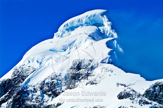 Ice and snow cliffs and overhangs cap the summit of a rugged mountain. Prospect Point, Crystal Sound, Antarctic Peninsula, Antarctic Circle, Antarctica.