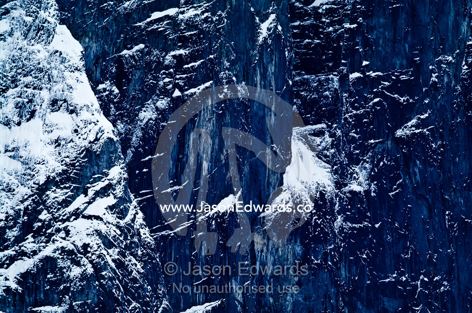 A rugged sheer black mountain cliff face covered in snow and ice. Fish Islands, Flouder Island, The Minnows, Crystal Sound, Antarctic Peninsula, Antarctic Circle, Antarctica.