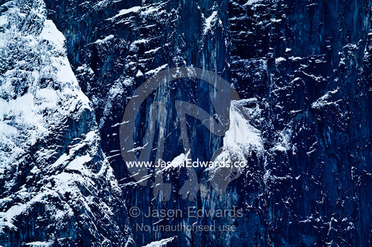 A rugged sheer black mountain cliff face covered in snow and ice. Fish Islands, Flouder Island, The Minnows, Crystal Sound, Antarctic Peninsula, Antarctic Circle, Antarctica.