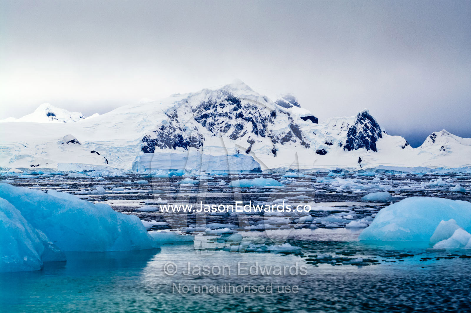 Crushed ice and fractured icebergs on a sea beneath a mountain range. Fish Islands, Flouder Island, The Minnows, Crystal Sound, Antarctic Peninsula, Antarctic Circle, Antarctica.