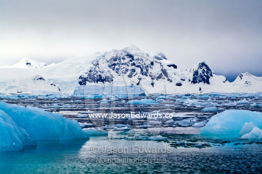 Crushed ice and fractured icebergs on a sea beneath a mountain range. Fish Islands, Flouder Island, The Minnows, Crystal Sound, Antarctic Peninsula, Antarctic Circle, Antarctica.