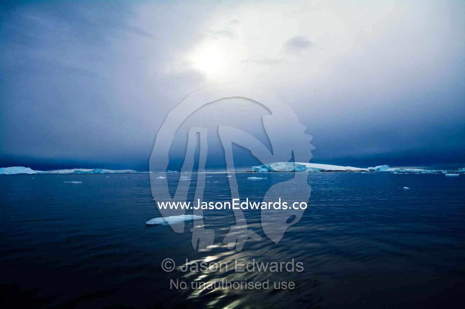 The sun casts ghostly reflected light over the surface of a calm sea. Fish Islands, Flouder Island, The Minnows, Crystal Sound, Antarctic Peninsula, Antarctic Circle, Antarctica.