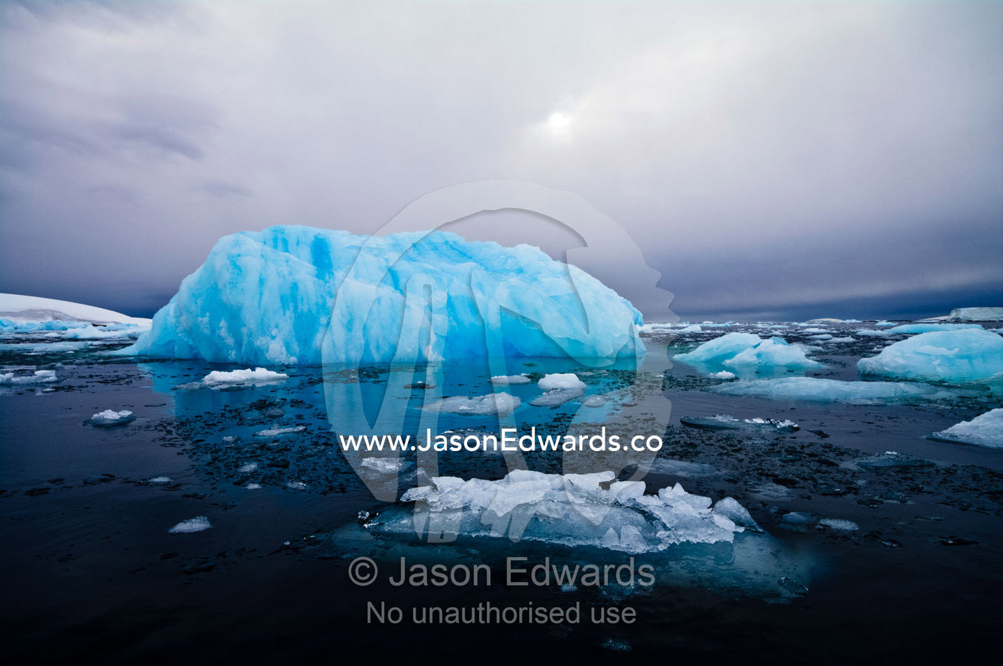 The sun casts ghostly reflected light over an iridescent blue iceberg. Fish Islands, Flouder Island, The Minnows, Crystal Sound, Antarctic Peninsula, Antarctic Circle, Antarctica.