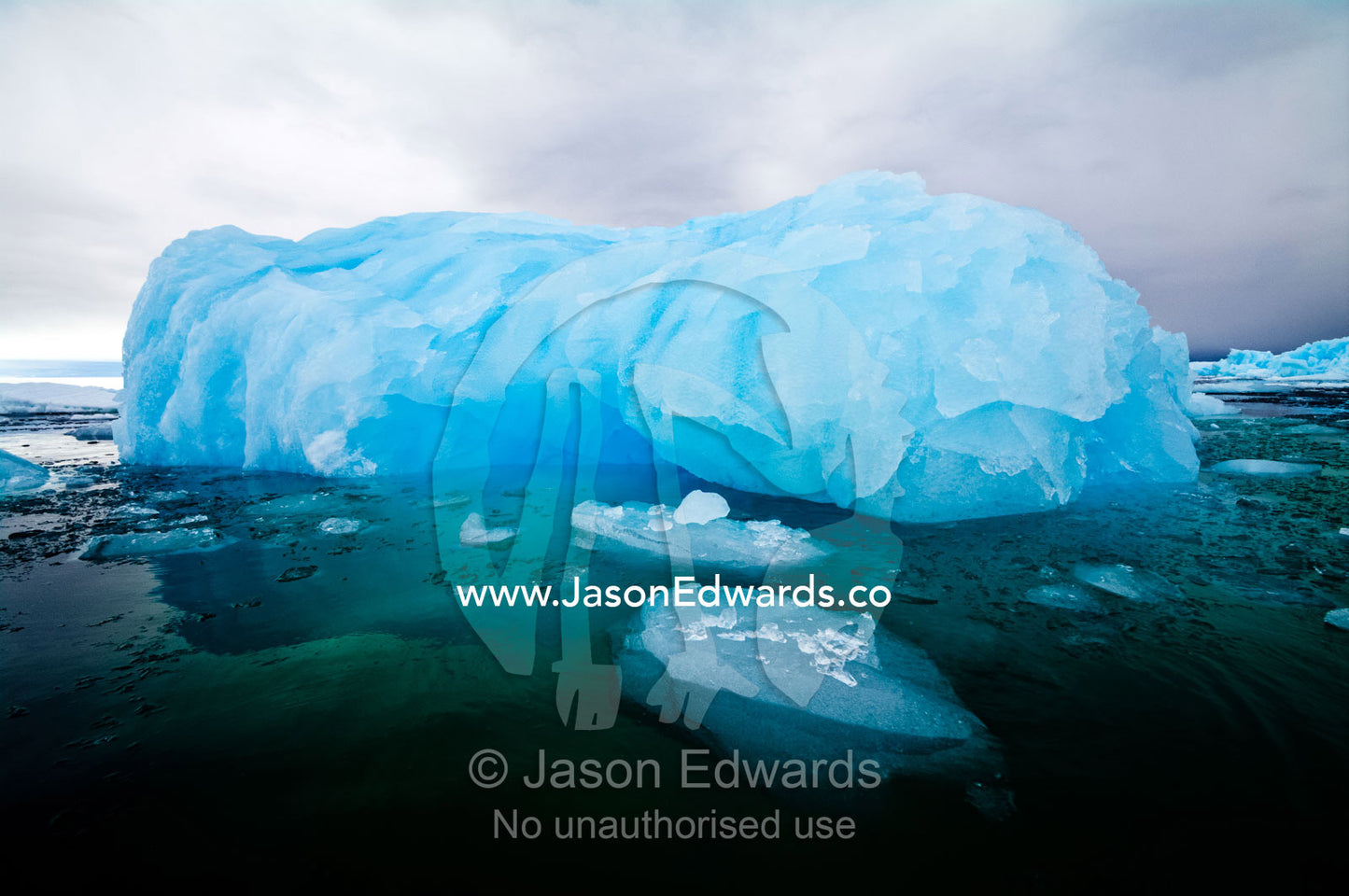 A ghostly grey storm washes over an iridescent blue iceberg in a bay. Fish Islands, Flouder Island, The Minnows, Crystal Sound, Antarctic Peninsula, Antarctic Circle, Antarctica.