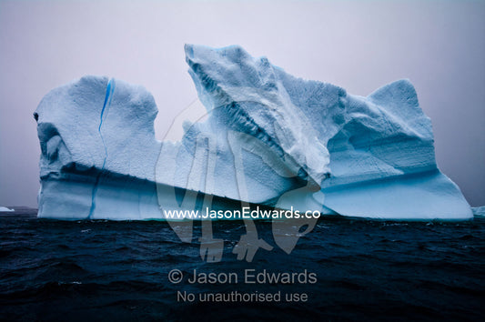 Jagged icebergs rise from a deep dark sea beneath a bitter grey sky. Pl��neau and Booth Islands, Bellingshausen Sea, Antarctic Peninsula, Antarctica.
