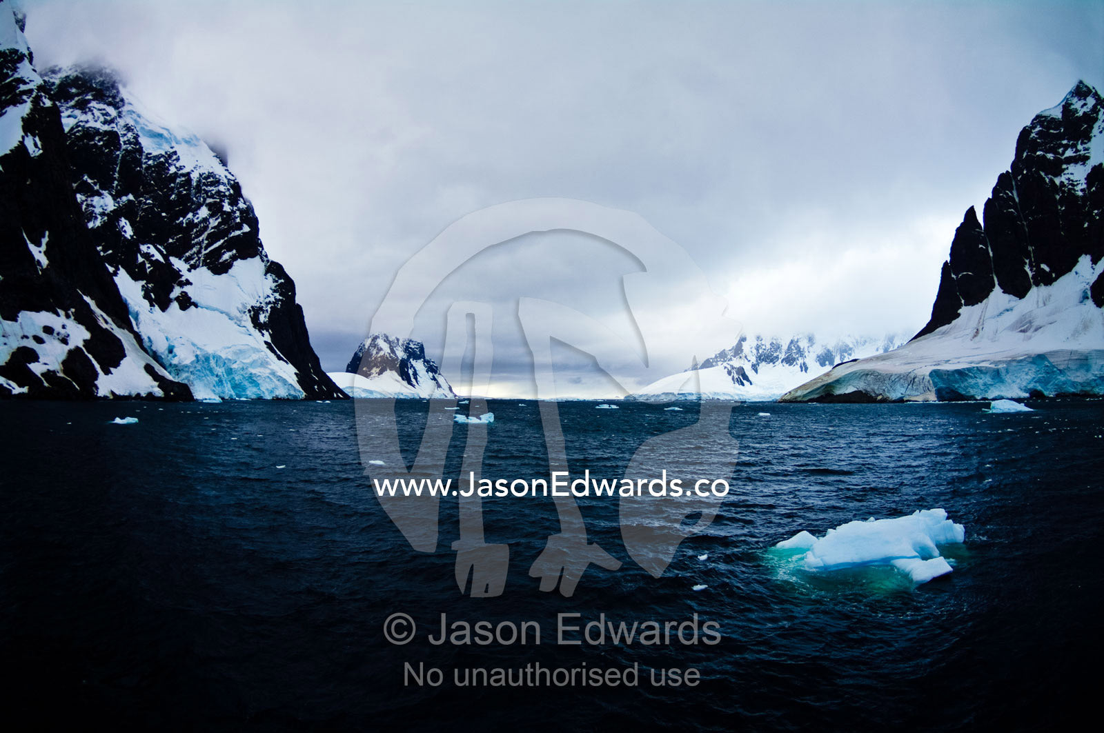 Gale force winds drive icebergs between massive stormy mountain peaks. Lemaire Channel, Antarctic Peninsula, Antarctica.