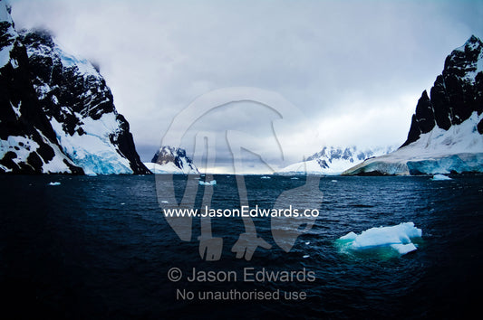 Gale force winds drive icebergs between massive stormy mountain peaks. Lemaire Channel, Antarctic Peninsula, Antarctica.
