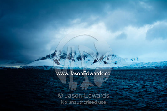 A dark brooding ocean channel between massive stormy mountain peaks. Lemaire Channel, Antarctic Peninsula, Antarctica.