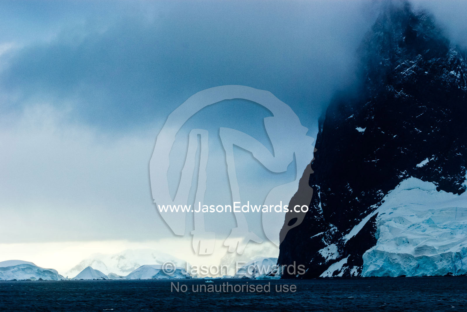A dark brooding ocean channel between massive stormy mountain peaks. Lemaire Channel, Antarctic Peninsula, Antarctica.