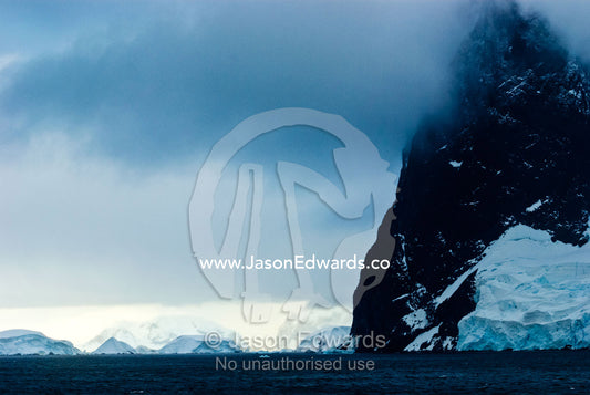 A dark brooding ocean channel between massive stormy mountain peaks. Lemaire Channel, Antarctic Peninsula, Antarctica.