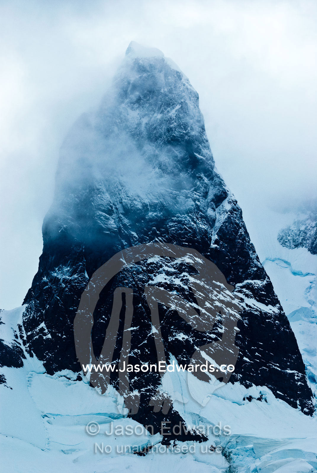 A dark brooding storm descends on a massive jagged mountain peak. Lemaire Channel, Antarctic Peninsula, Antarctica.