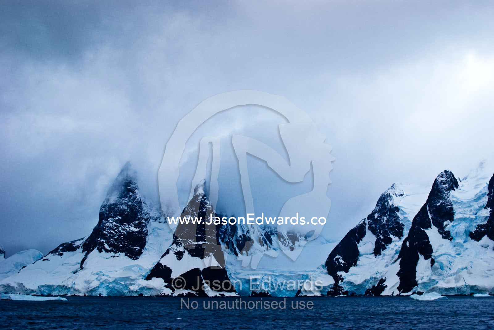 A dark brooding ocean channel between massive stormy mountain peaks. Lemaire Channel, Antarctic Peninsula, Antarctica