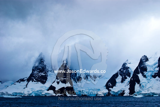 A dark brooding ocean channel between massive stormy mountain peaks. Lemaire Channel, Antarctic Peninsula, Antarctica