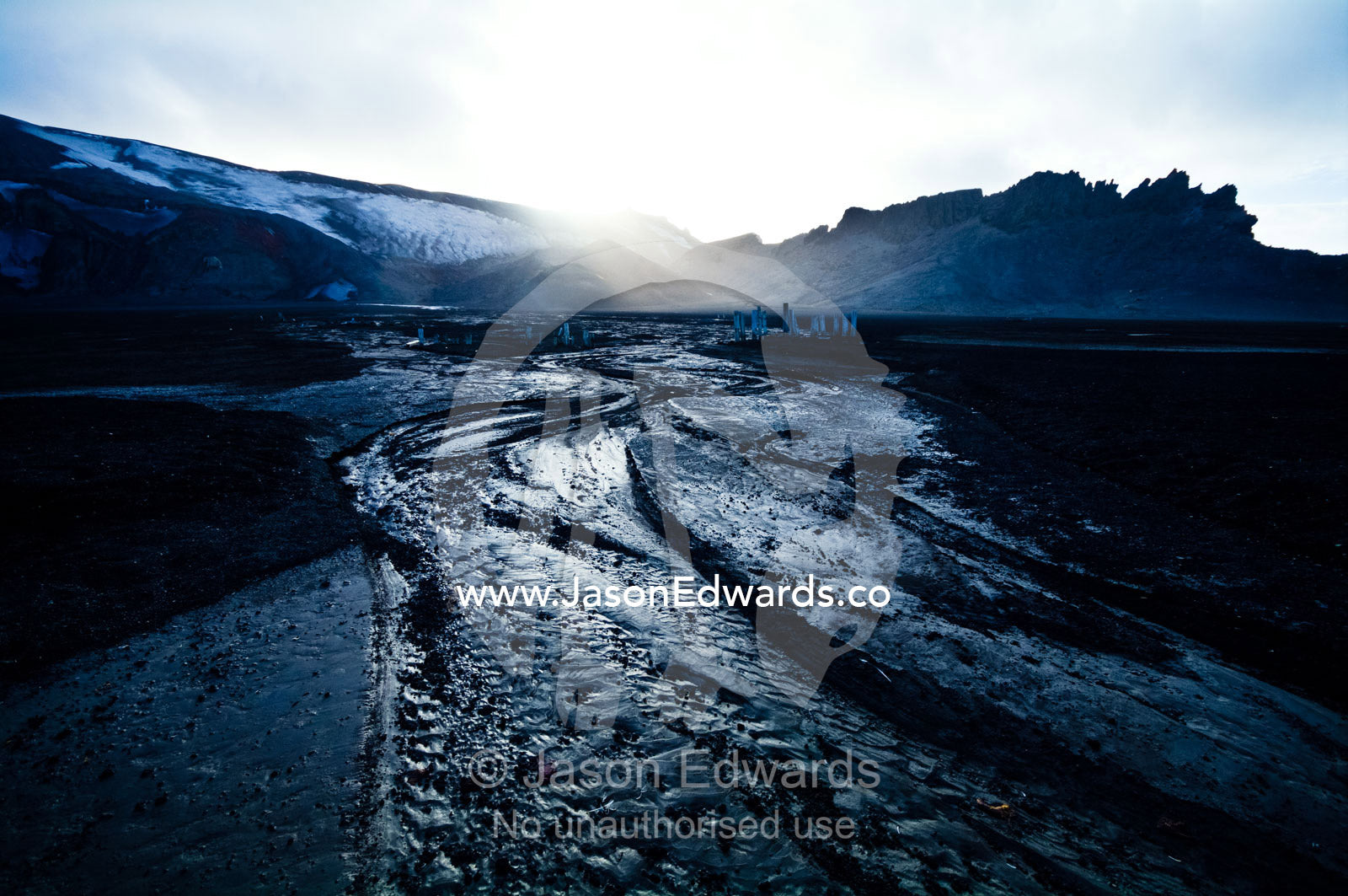 Ice melt forms streams that carve through black volcanic sand beaches. Whalers Bay, Port Foster, Deception Island, South Shetland Islands, Antarctic Peninsula, Antarctica.