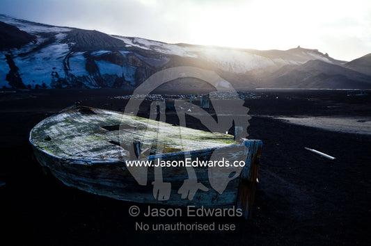 Antique timber whaling boat ruins stranded in black volcanic sand. Hektor Whaling Station, Whalers Bay, Port Foster, Deception Island, South Shetland Islands, Antarctic Peninsula, Antarctica.