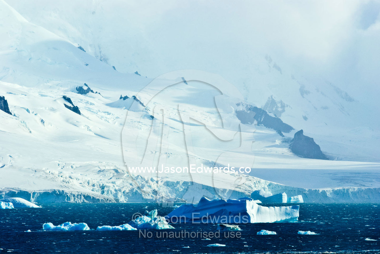 Icebergs float past rugged ice-covered mountain peaks and glaciers. Half Moon Island, Burgas Peninsula, Livingston Island, Errera Channel, South Shetland Islands, Antarctic Peninsula, Antarctica.