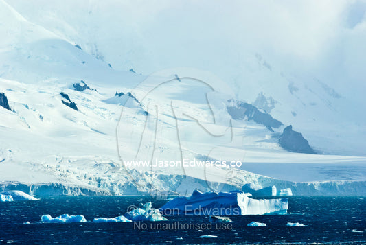 Icebergs float past rugged ice-covered mountain peaks and glaciers. Half Moon Island, Burgas Peninsula, Livingston Island, Errera Channel, South Shetland Islands, Antarctic Peninsula, Antarctica.
