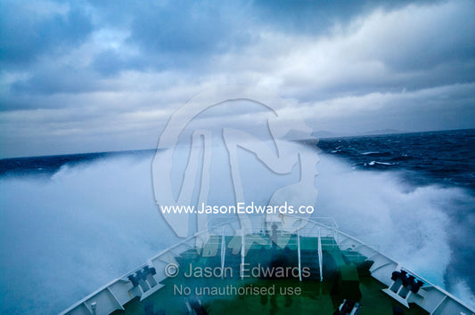 A ships bow ploughs through huge waves rounding treacherous Cape Horn. Cape Horn, Tierra del Fuego, Hornos Island, Chile. The Drake Passage between the Atlantic Ocean and Pacific Ocean.