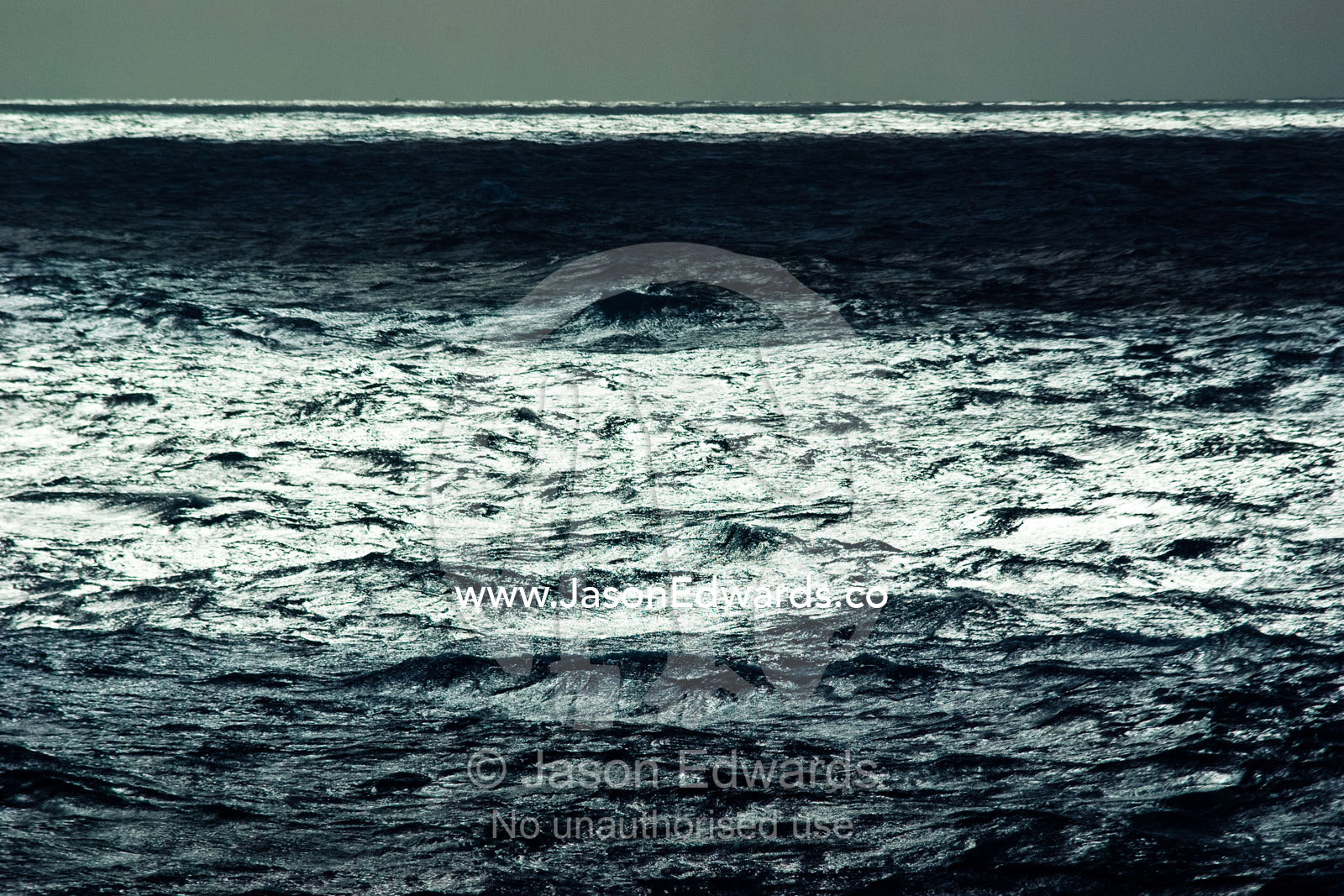 Sunbeams pierce a grey clouds on a stormy featureless ocean horizon. The Drake Passage between the Atlantic Ocean and Pacific Ocean.