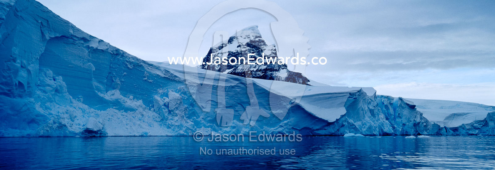 A sheer black mountain summit covered in snow and ice above a glacier. Fish Islands, The Minnows, Flounder Island, Crystal Sound, Antarctic Peninsula, Antarctic Circle, Antarctica.