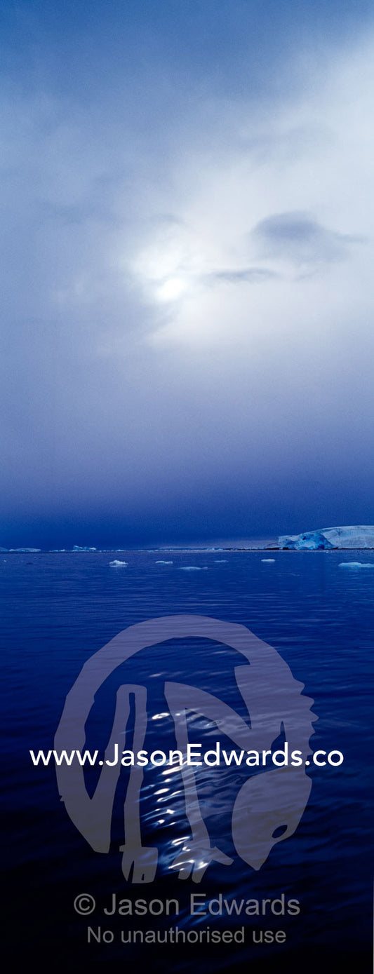 The sun casts ghostly reflected light over the surface of a calm sea. Fish Islands, The Minnows, Flounder Island, Crystal Sound, Antarctic Peninsula, Antarctic Circle, Antarctica.