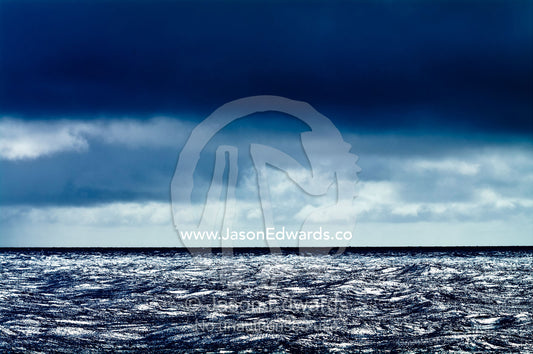 A dark, menacing storm descends over a calm silvery ocean surface. Vava'u Island Group, Pacific Ocean, Oceania, Kingdom of Tonga.