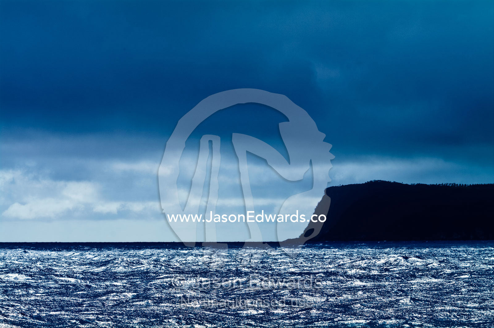 A dark, menacing storm descends over a silvery ocean and headland. Vava'u Island Group, Pacific Ocean, Oceania, Kingdom of Tonga.