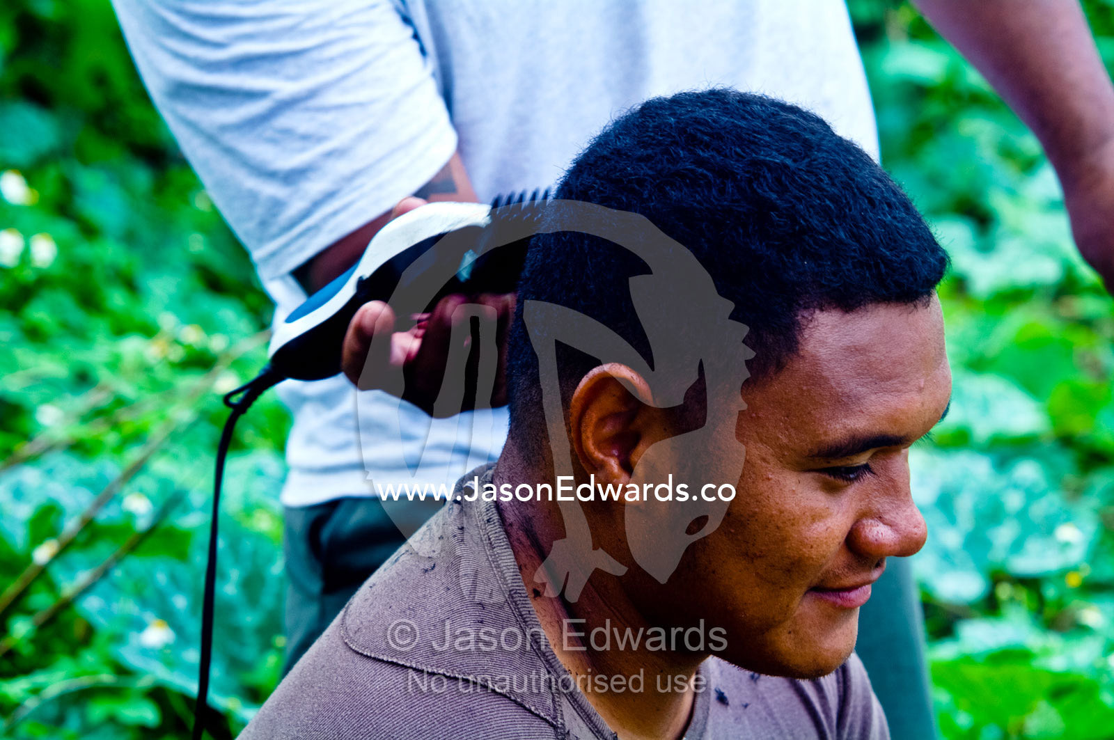 A Tongan man receives a haircut from a friend with shaving clippers. Port of Refuge, Neiafu, Vava'u Island Group, Pacific Ocean, Oceania, Kingdom of Tonga.